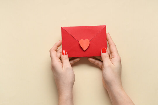 Female hands with red manicure and envelope on beige background. Valentine's Day celebration