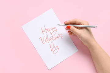 Female hands with red manicure, pen and festive postcard on pink background. Valentine's Day...