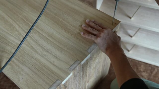 In the process of furniture assembly, two flat parts are joined together using chopsticks. Tools involved include a hammer, saw, and drill.