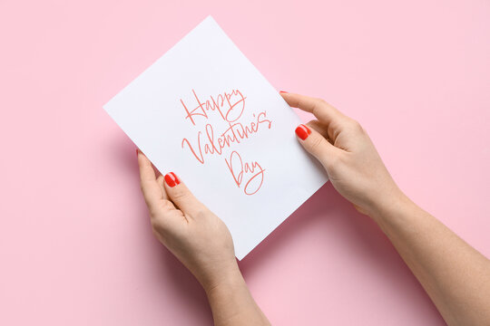 Female hands with red manicure and festive postcard on pink background. Valentine's Day celebration