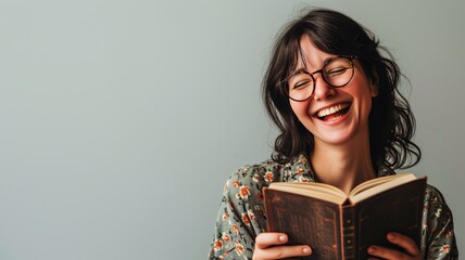 A woman laughs joyfully while reading a book - obrazy, fototapety, plakaty
