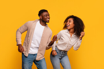 Obraz premium Cheerful African American couple dancing and laughing together on yellow backdrop