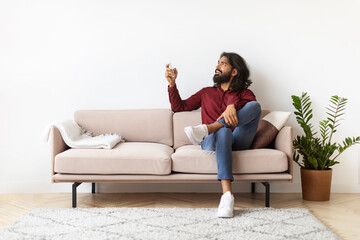 Obraz premium Relaxed millennial Indian man turning on AC at home