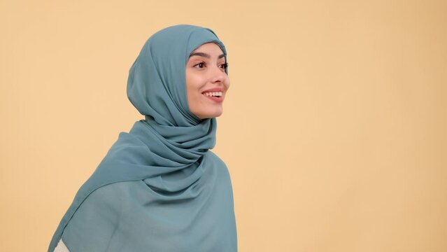 Bewildered Arab woman exclaims Wow, expression filled with amazement, against a serene beige background, capturing a scene infused with genuine astonishment and joy.