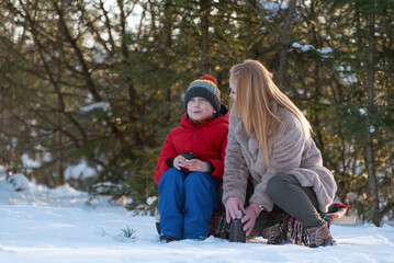 Young mother and children son in winter forest. Family trip out of town. Picnic in the snowy forest.