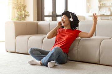 Young black woman wearing wireless headphones dancing to music at home