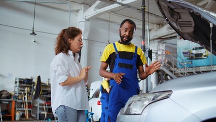 Qualified serviceman in repair shop showing customer what needs to be changed on her car for it to...