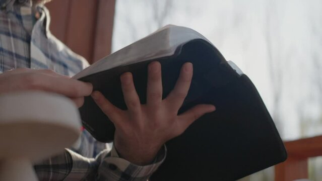 Young man sitting on front porch reading his Bible and drinking coffee