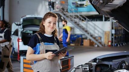 Portrait of smiling mechanic in repair shop using tablet to check car performance parameters during maintenance. Happy garage workplace employee using device to examine damaged vehicle