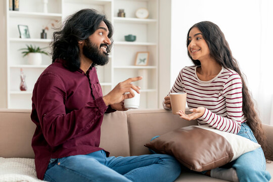 Positive millennial indian couple drinking coffee at home