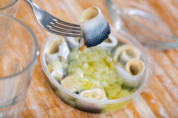 Round plastic bowl containing pickled herring fillet with necessary table laying
