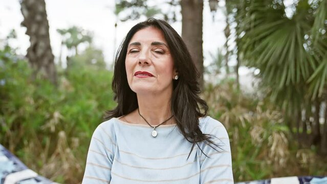 Mature hispanic woman outdoors, looking thoughtful in a serene park setting.