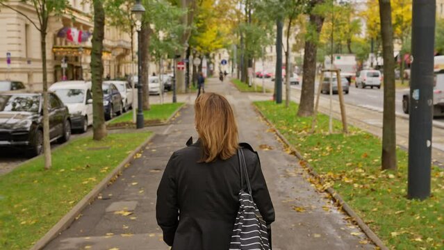 Following behind woman walking on city treelined sidewalk on Ringstrasse, Ring Road, in downtown Vienna, Austria