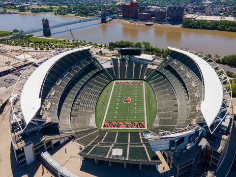 Aerial view of the Paycor Stadium, empty. Bengals logo on green turf. J ohn A. Roebling Suspension Bridge in the background over the Ohio River.
