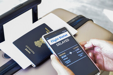 Woman hand holding her mobile phone displaying delayed flight status information. Travel concept...