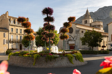 Scenic cityscape of Sisteron overlooking fountain in brightly blooming flowers in front of medieval...