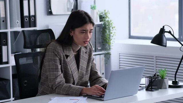 Saddened Caucasian woman diligently works with laptop in the office. This image reflects the resilience and determination she displays while navigating challenges in the professional realm.
