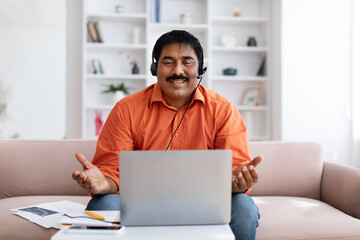 Fototapeta na wymiar Positive mature indian man working from home, using laptop, headset