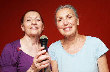 two elderly female friends with microphone, laughs and prepares for party karaoke over red...