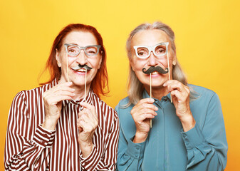 funny elderly female friends with fake mustache and glasses, laughs and prepares for party