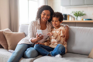 Happy African American Mom And Little Son Relaxing With Smartphone At Home - obrazy, fototapety, plakaty