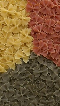 Italian tricolore farfalle pasta background with separated colours.  Table spin. Vertical video.