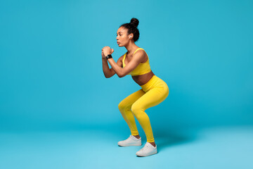Fit African American Lady Doing Deep Squat Exercise, Blue Background
