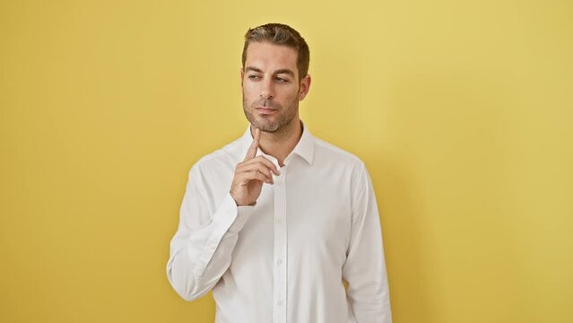 Chuffed young hispanic man smiling and pointing fingers up, hit with a bright idea or puzzling question, standing alone against a yellow background. a real head-scratcher!
