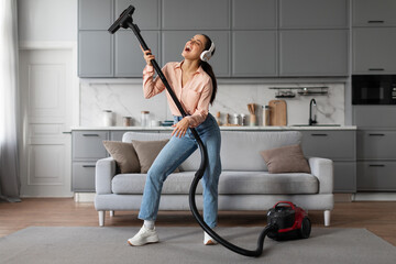 Joyful woman using vacuum cleaner as a mic for fun