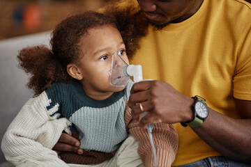 Medium shot of African American little girl doing inhalation with nebulizer mask in hands of father