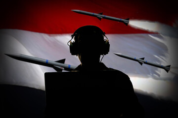 Silhouette of a military man wearing headphones behind a laptop against a background of the Yemeni flag and flying missiles, contour lighting.  - obrazy, fototapety, plakaty