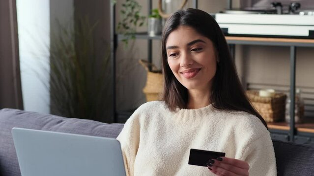 Caucasian woman uses laptop and credit card to make a purchase. This image illustrates the integration of technology and commerce, showcasing the living room as a space for secure online transactions.
