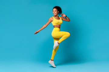 Fototapeta na wymiar black woman in sportswear jumping doing exercise on blue backdrop