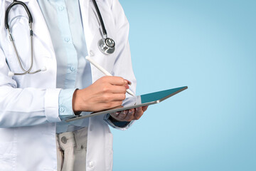 Woman doctor writing on tablet, close-up, blue background