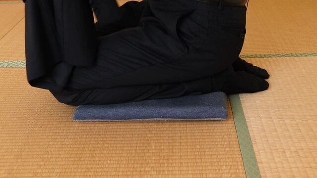 畳の上に上着を置いて座布団に正座で座るスーツ姿の男性	