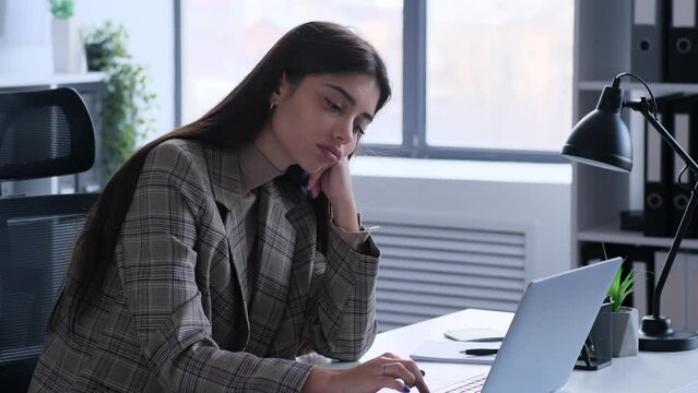 Experiencing boredom, a businesswoman sits at office desk during work. This image captures the lack of engagement and monotony she feels, highlighting the challenges of maintaining focus and interest.