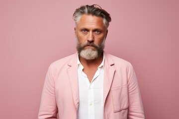 Portrait of a handsome mature man with gray beard and mustache, dressed in a pink jacket and white shirt, isolated over pink background.