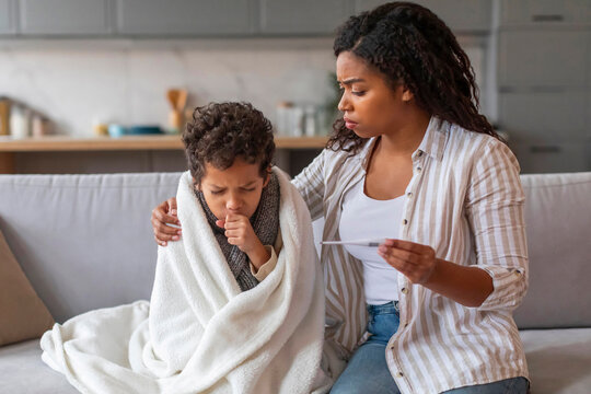 Worried black mother holding thermometer and looking at her coughing son