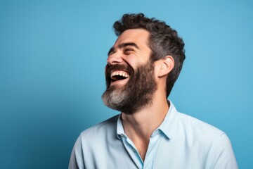 Handsome man with long beard laughing and looking up on blue background