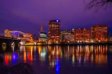 Hartford Skyline at night over the Connecticut River, a vibrant cityscape along Riverfront Park, lighted Riverwalk trail, and Founders Bridge in the capital city of Connecticut State, United States