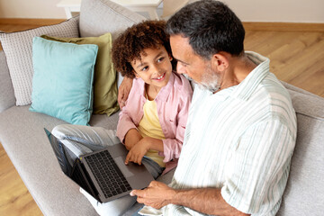 Hispanic grandpa and grandson browsing on laptop in living room