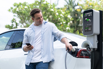 Modern eco-friendly man recharging electric vehicle from EV charging station, using Innovative EV...