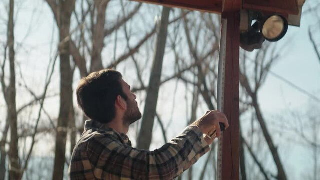 Young male contractor taking measurements of house exterior