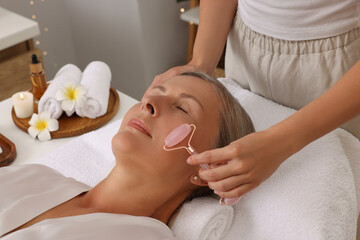 Obraz na płótnie Canvas Woman receiving facial massage with rose quartz roller in beauty salon, closeup