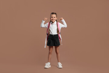 Fototapeta na wymiar Happy schoolgirl with backpack on brown background