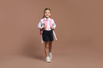 Fototapeta na wymiar Happy schoolgirl with backpack on brown background