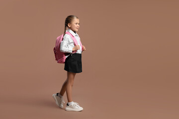 Fototapeta na wymiar Happy schoolgirl with backpack on brown background, space for text