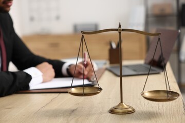 Lawyer working at table in office, focus on scales of justice