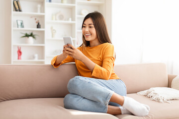 Positive millennial chinese lady messaging on phone at home