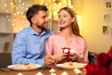 Man gazing at woman with gift, romantic dinner backdrop